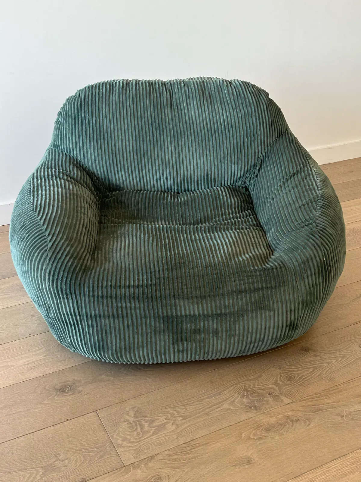 Phone photo of a green corduroy armchair on a timber floor