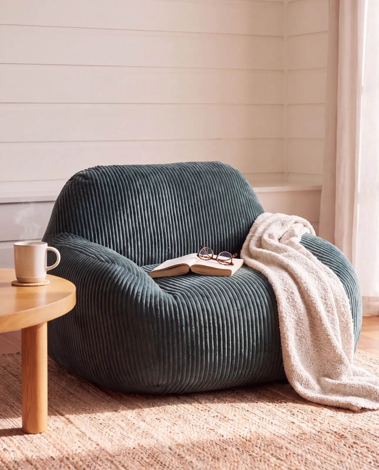 Green corduroy armchair beside a timber side table, with a book and a cream throw
